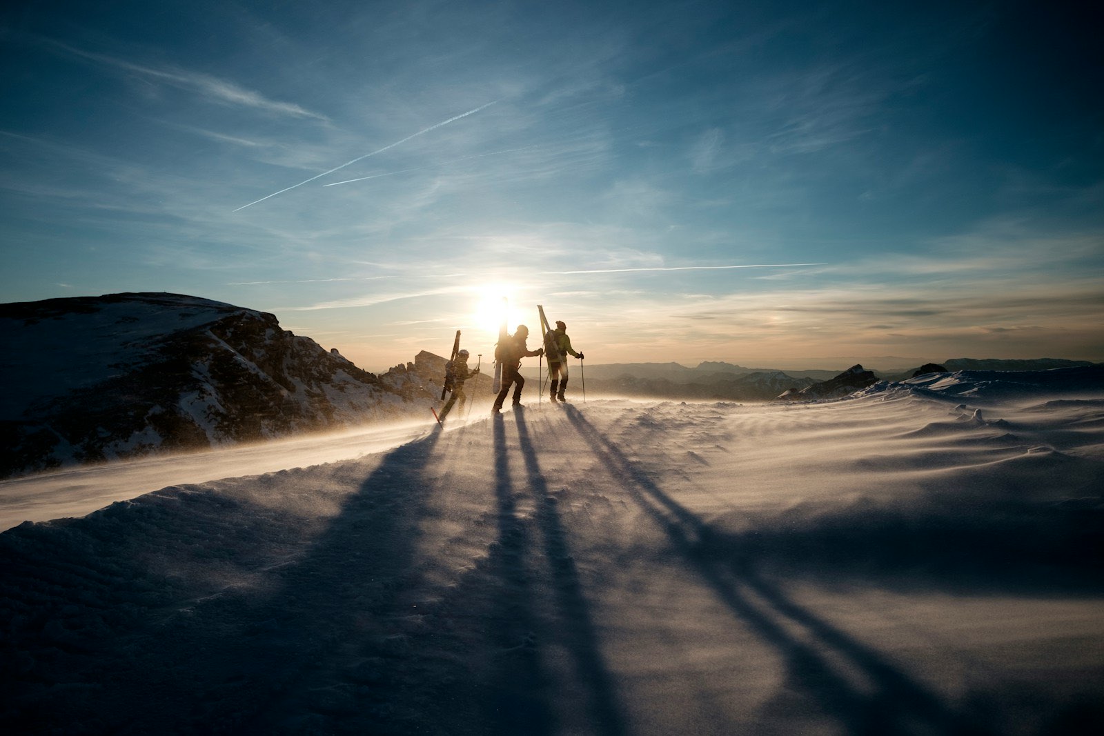 Ski tourers on a windy ridge silhouetted against the low sun